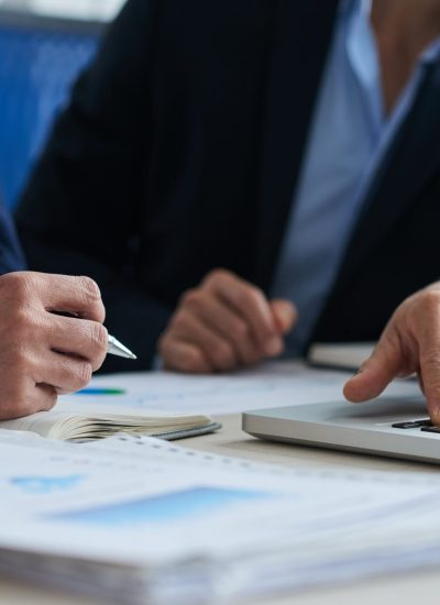 two-unrecognizable-male-colleagues-using-laptop-business-charts-lying-desk
